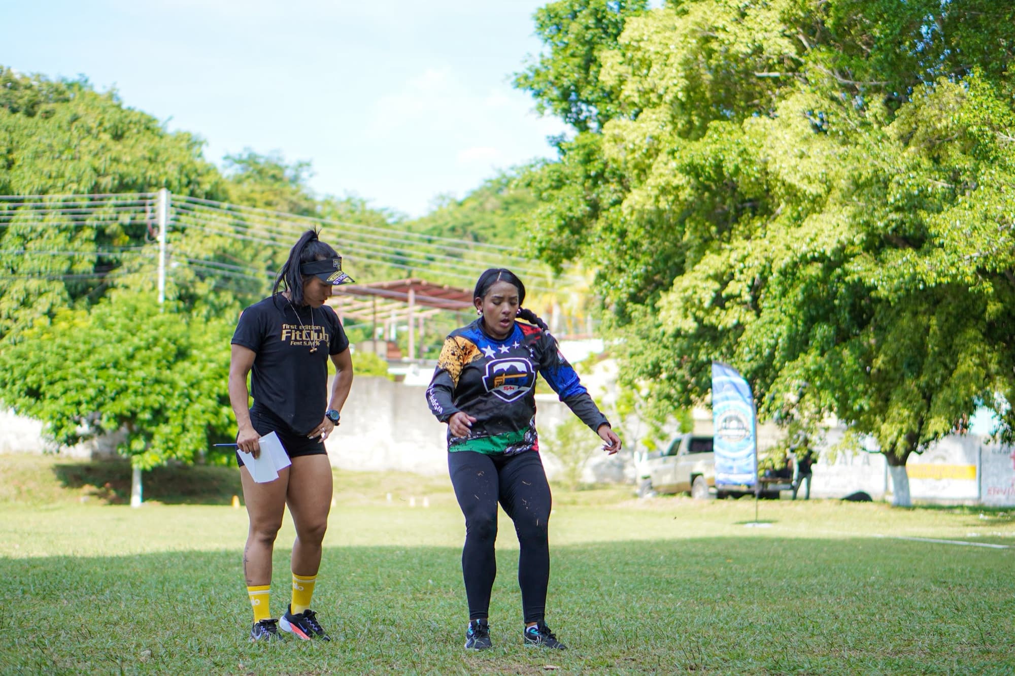 Coach de Fit Club acompañando a una atleta durante un ejercicio sobre la grama
